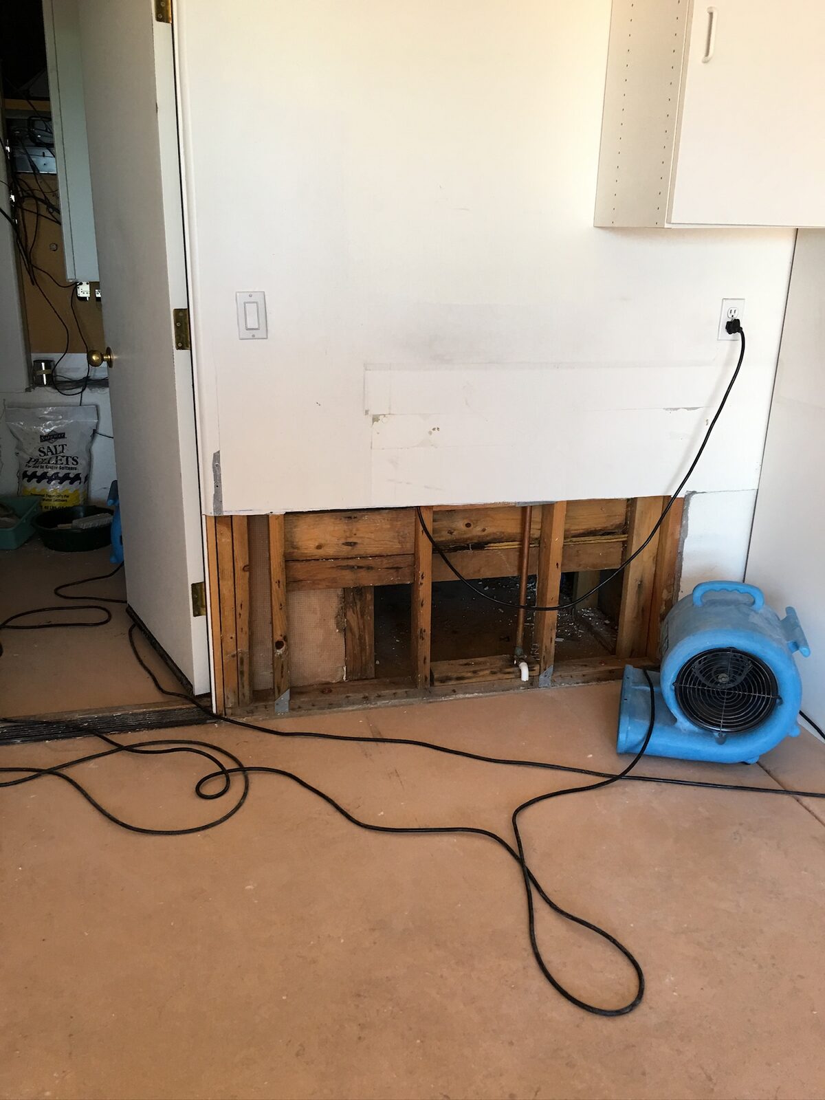 Air mover directed at a garage wall with lower drywall removed to expose framing