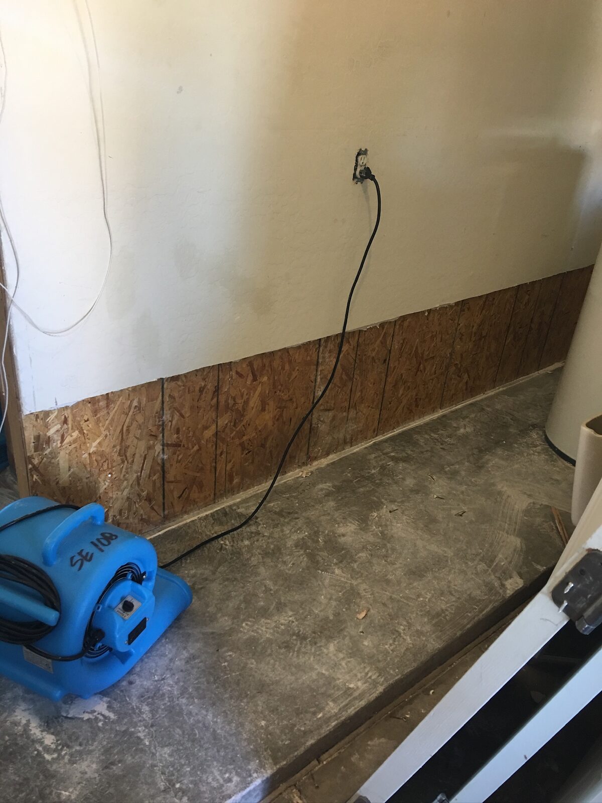 Air mover drying a corner where lower drywall was removed to expose sheathing
