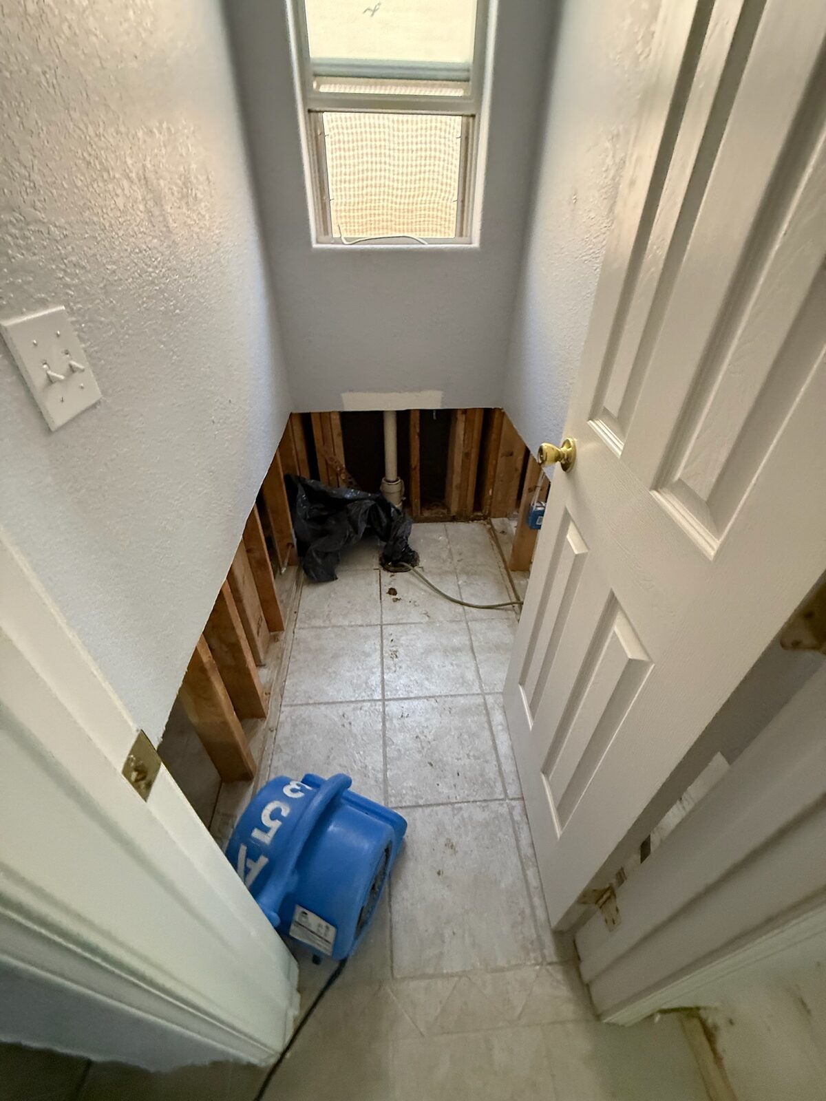 Air mover drying a small bathroom with lower drywall removed to the studs