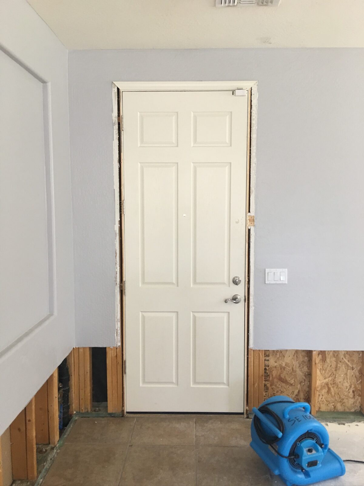 Air mover drying a wall with lower drywall removed beside a garage entry door