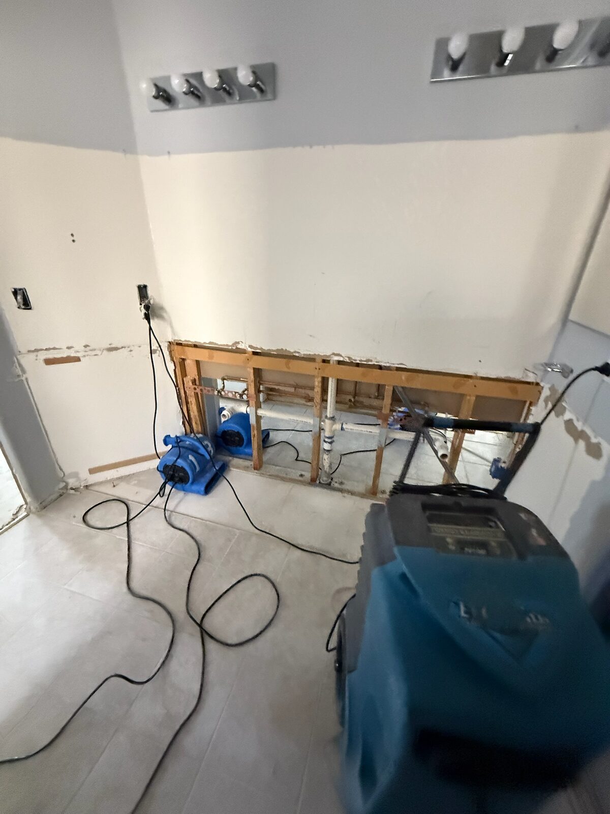 Air movers and a dehumidifier drying a bathroom wall opened to expose plumbing
