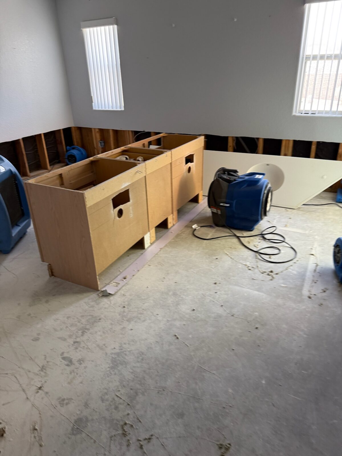 Air movers and a dehumidifier drying a room with lower drywall removed and cabinet boxes staged