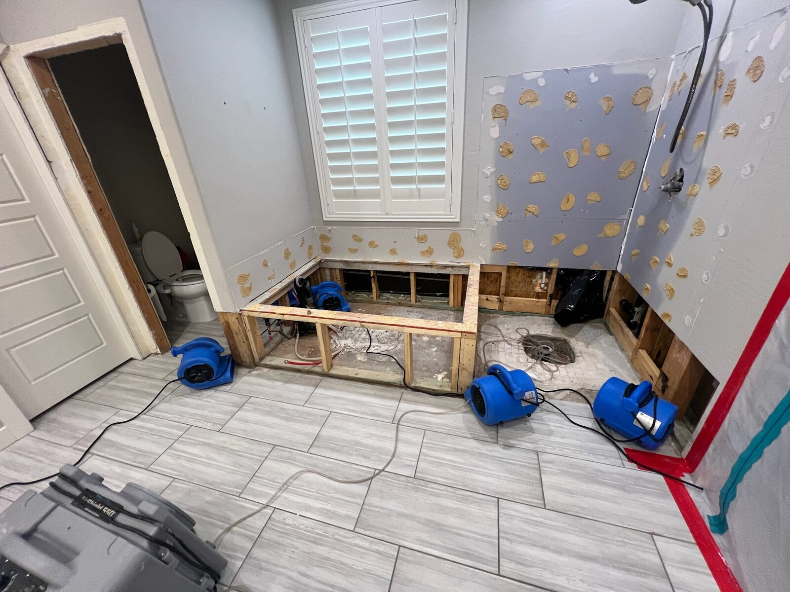 Air movers drying a bathroom with tub deck framing exposed and new drywall patched
