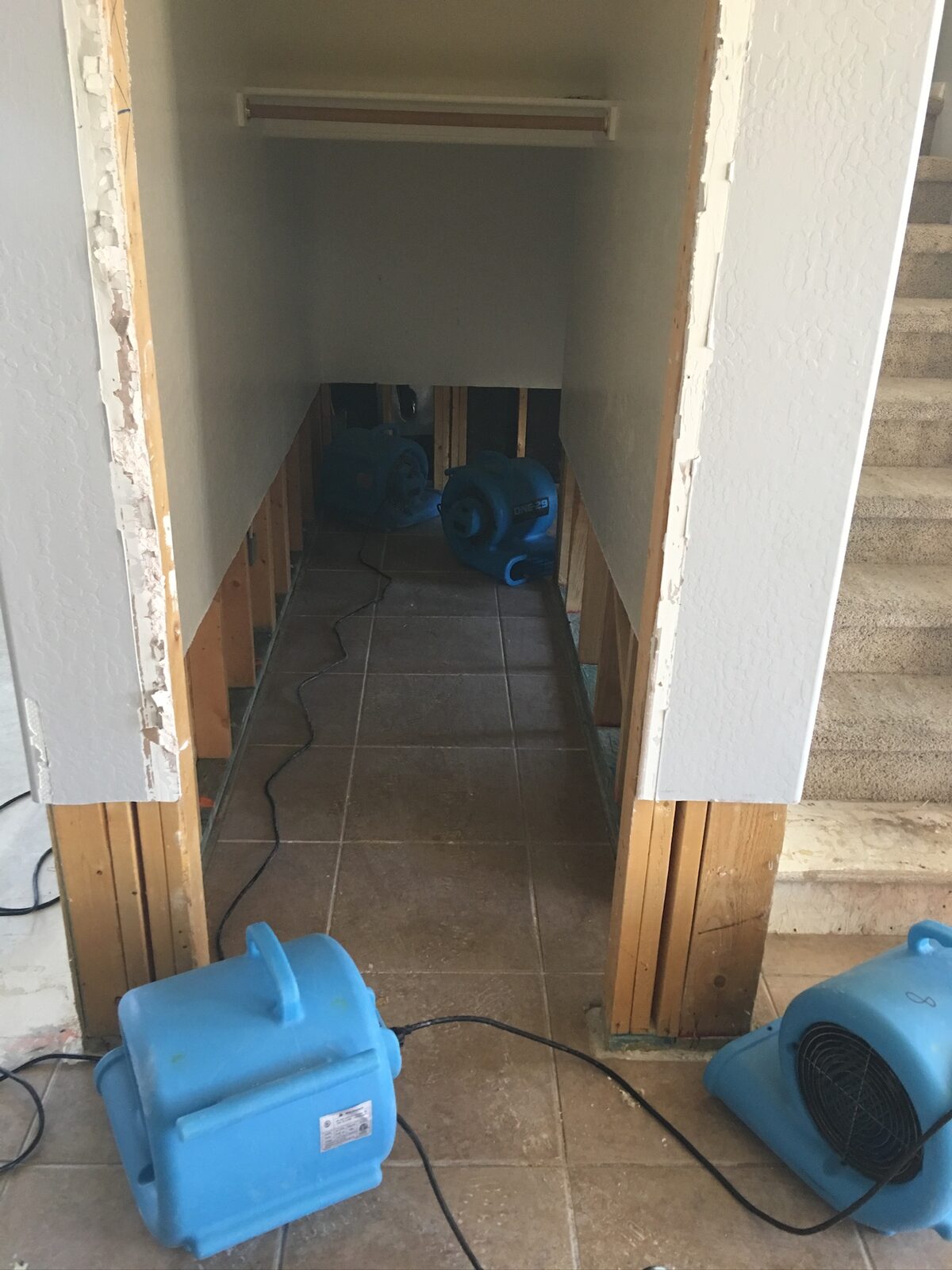 Air movers drying a hallway with lower walls cut back to the studs near a staircase