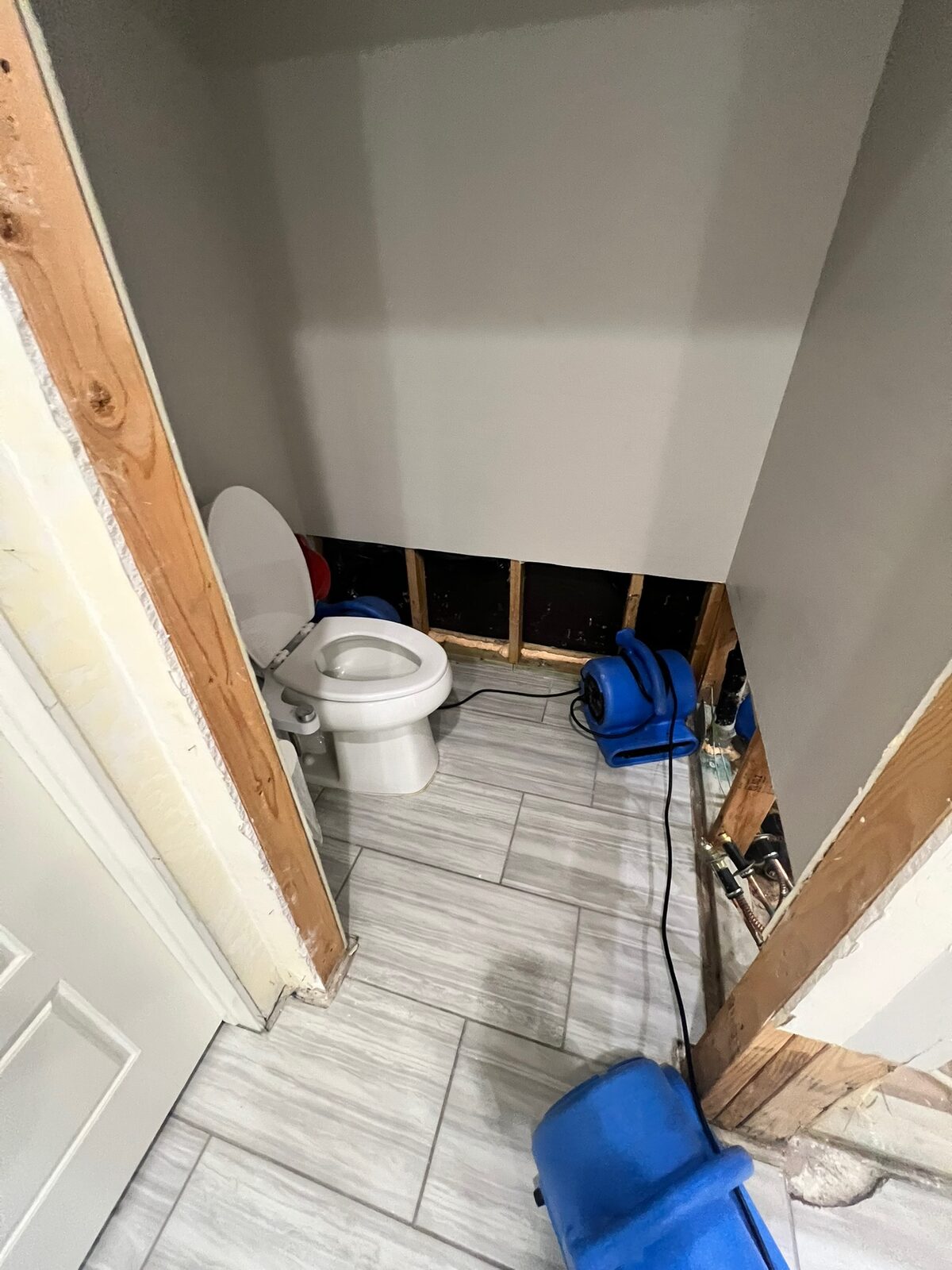 Air movers drying a small bathroom with lower drywall removed around the toilet