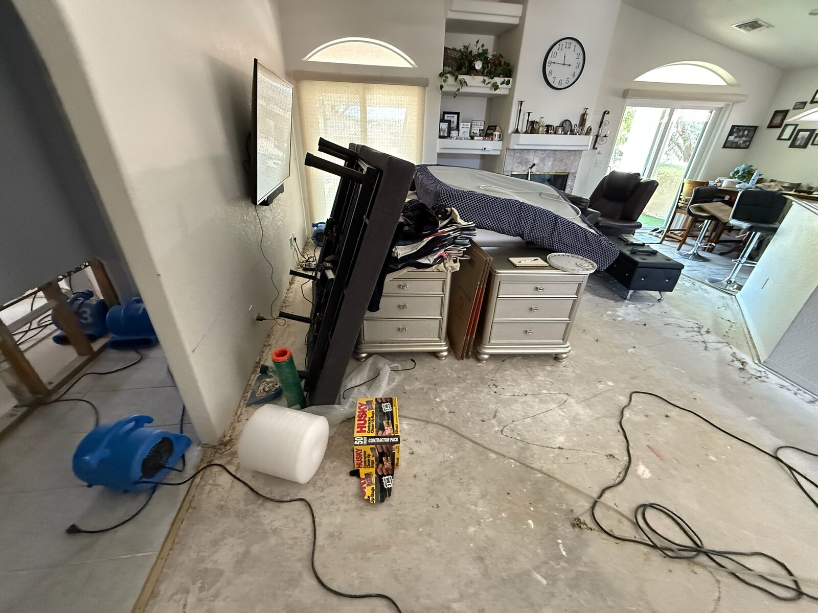 Air movers drying a stripped concrete floor in a living area with furniture moved aside