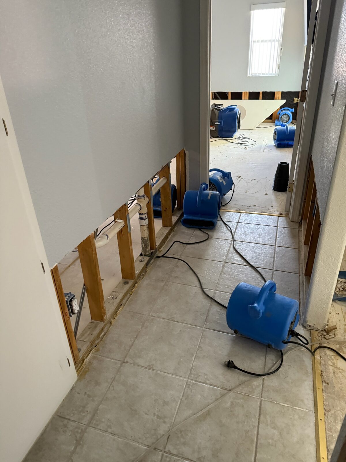 Air movers drying a tiled hallway with drywall removed along the base of the walls