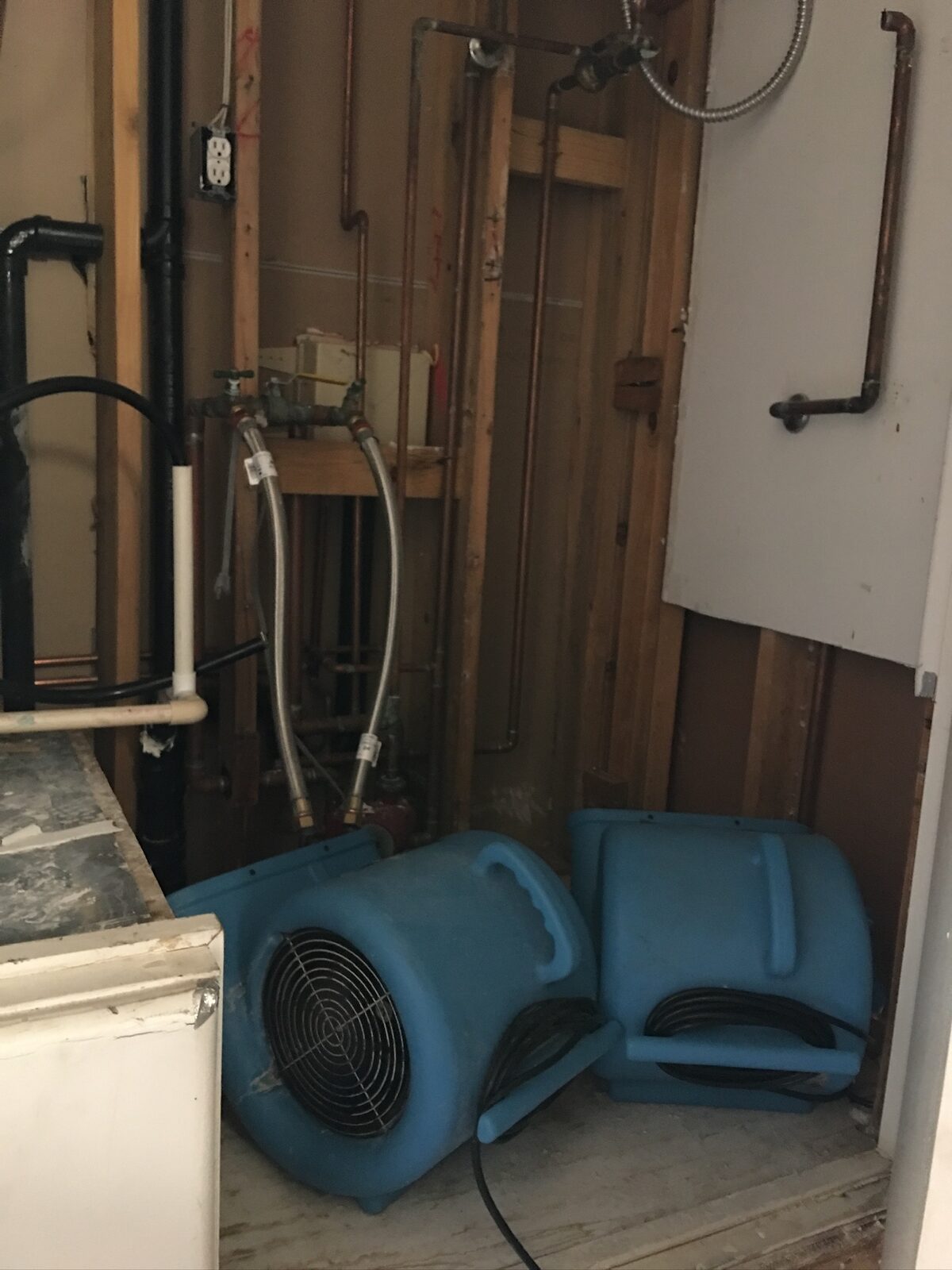 Air movers beside an opened wall showing copper supply lines and framing