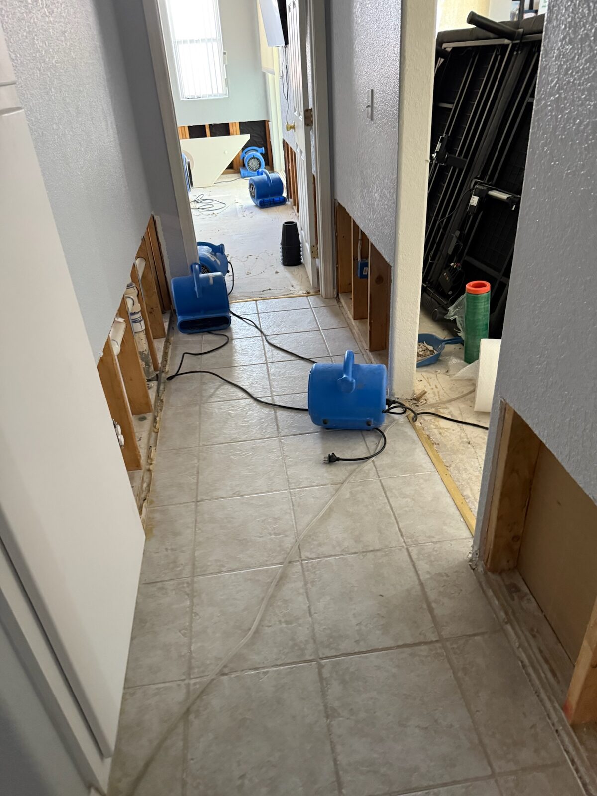 Air movers positioned along a tiled hallway with flood cut walls during drying