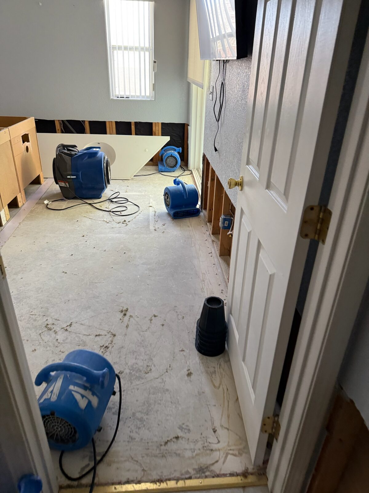 Air movers positioned in a bedroom where lower drywall was cut out around the walls