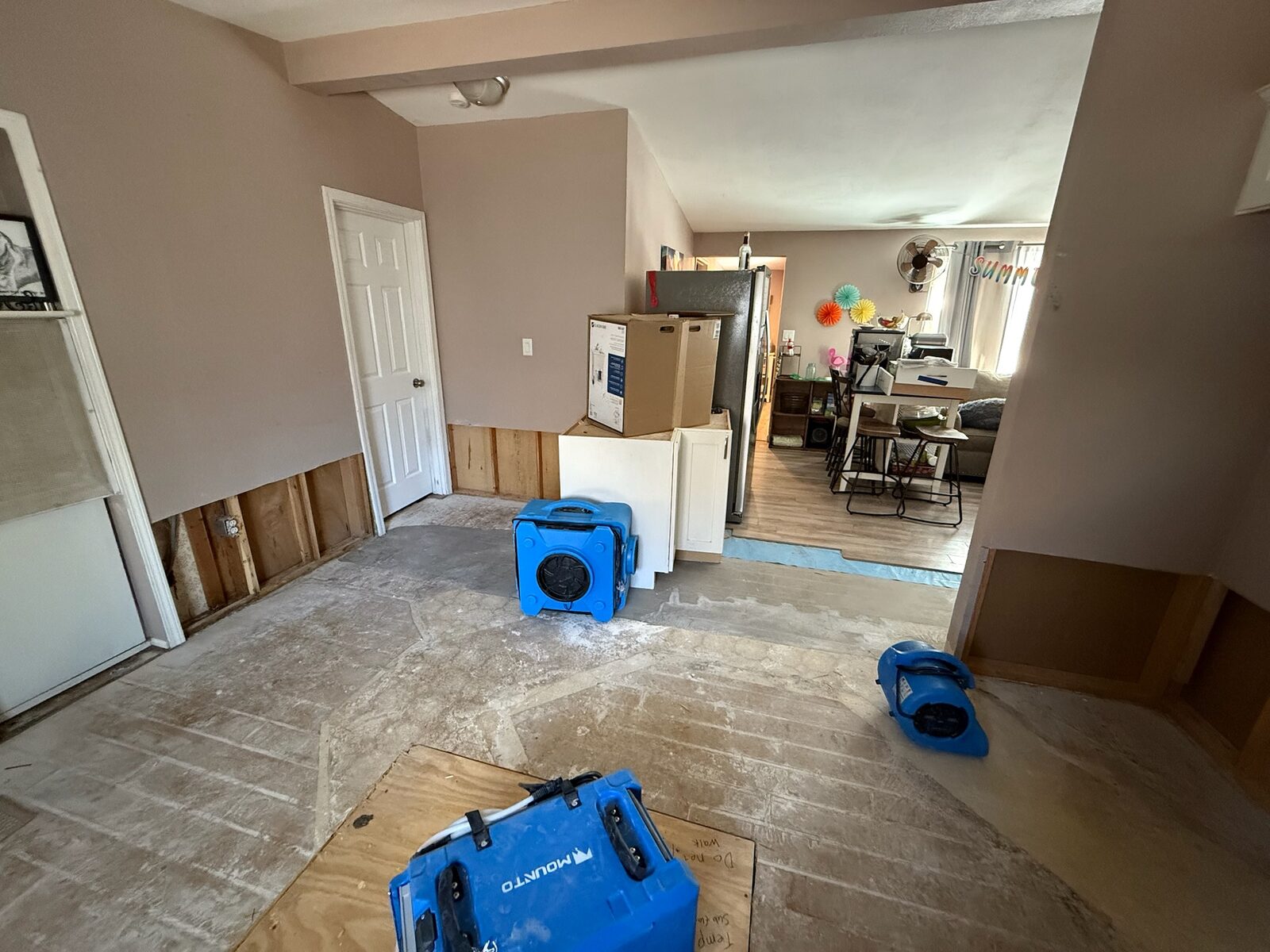 Air movers set on a bare subfloor beside walls with lower drywall removed