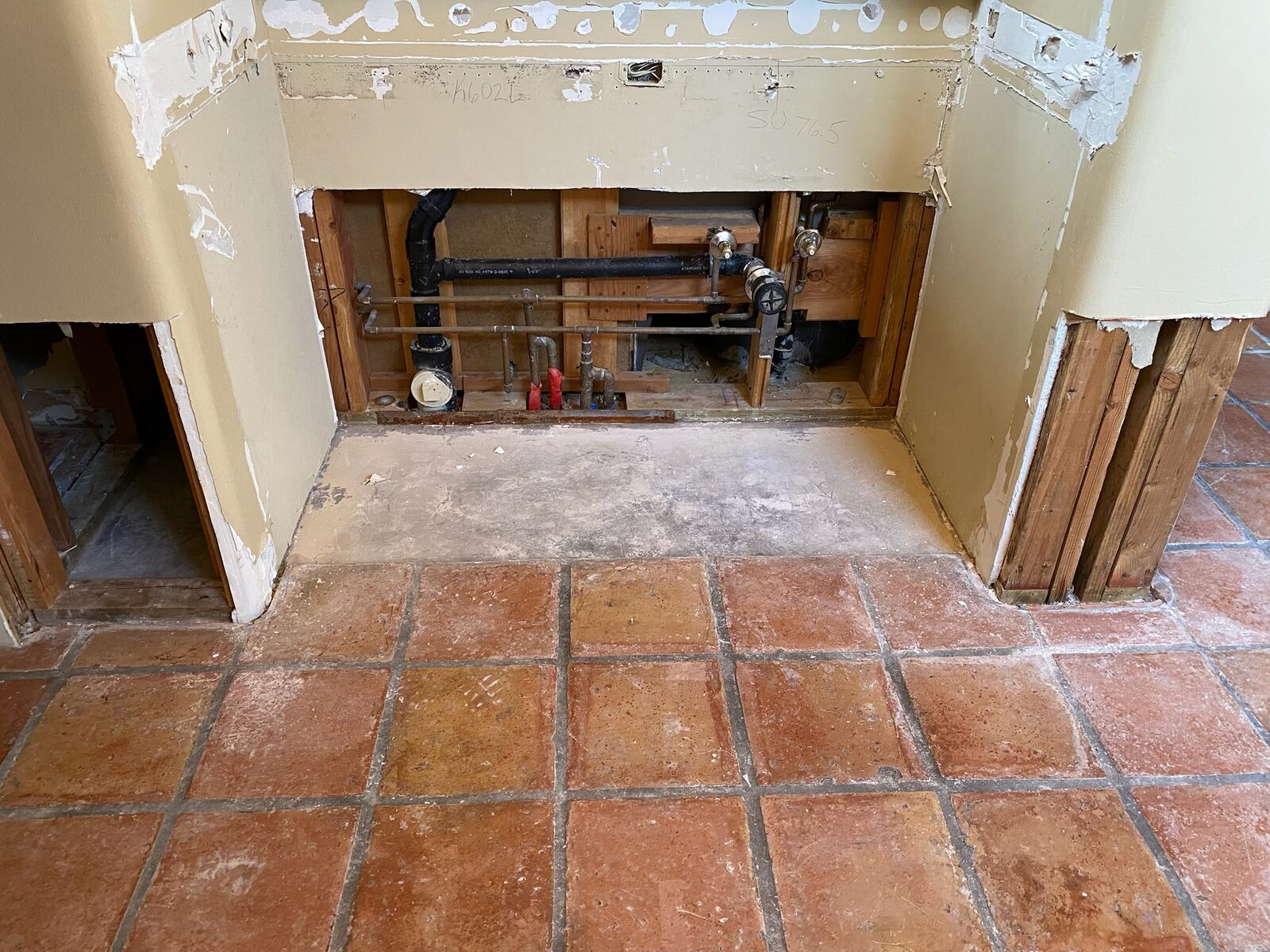 Base cabinets removed exposing wall plumbing above a saltillo tile floor