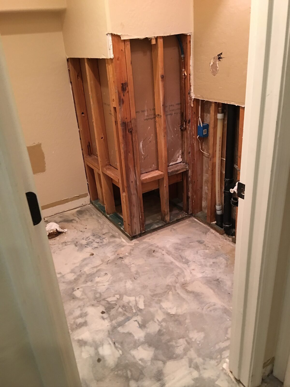 Bathroom stripped to studs showing shower framing and exposed subfloor