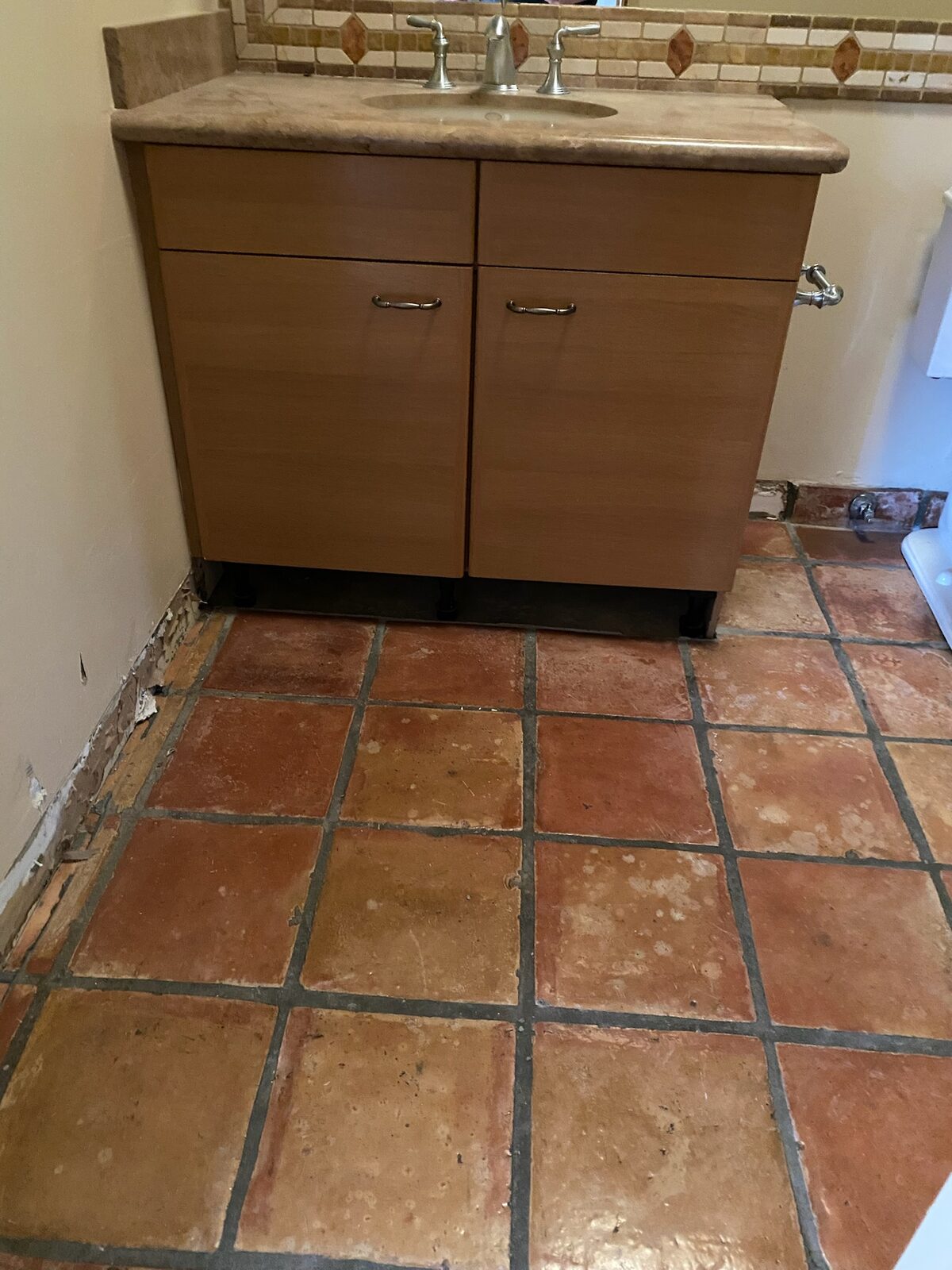 Bathroom vanity raised on supports with baseboard removed above saltillo tile during drying