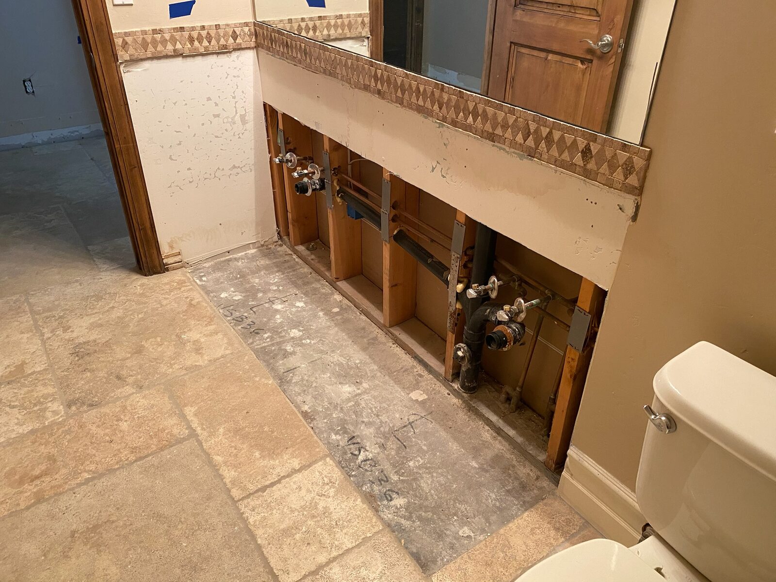 Bathroom vanity removed exposing supply valves and drain piping below a mirror