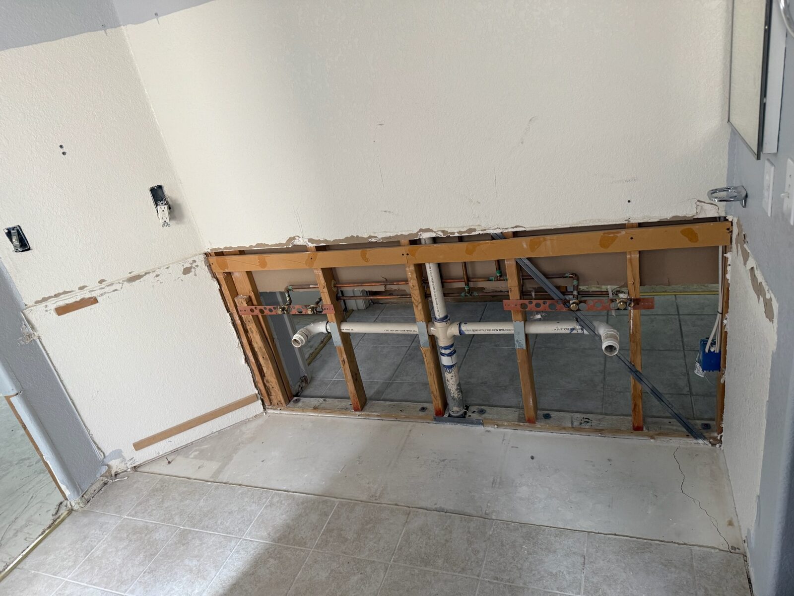 Bathroom wall opened to expose copper supply lines and PVC drain piping during repair