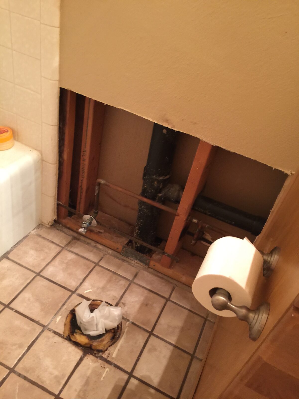 Bathroom wall opened to expose supply and drain lines with the toilet removed and flange visible