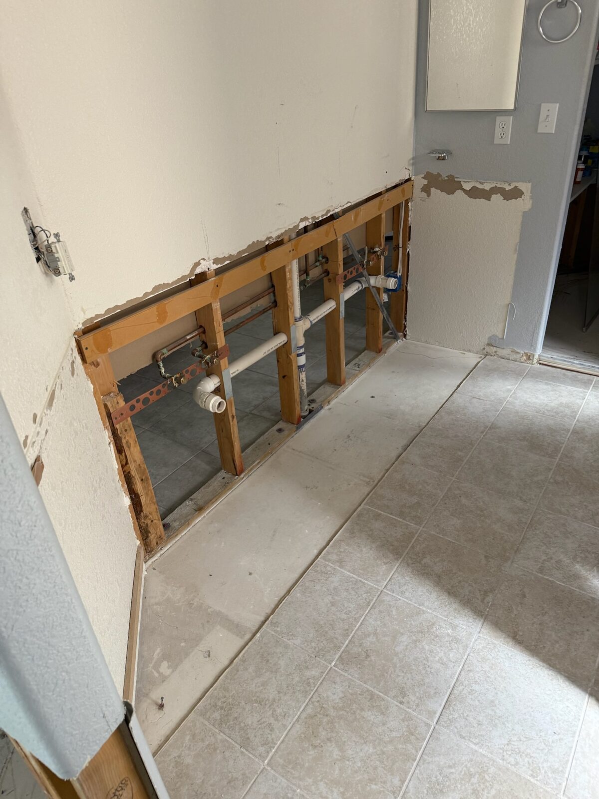 Bathroom wall opened to studs showing copper supply lines and drain plumbing