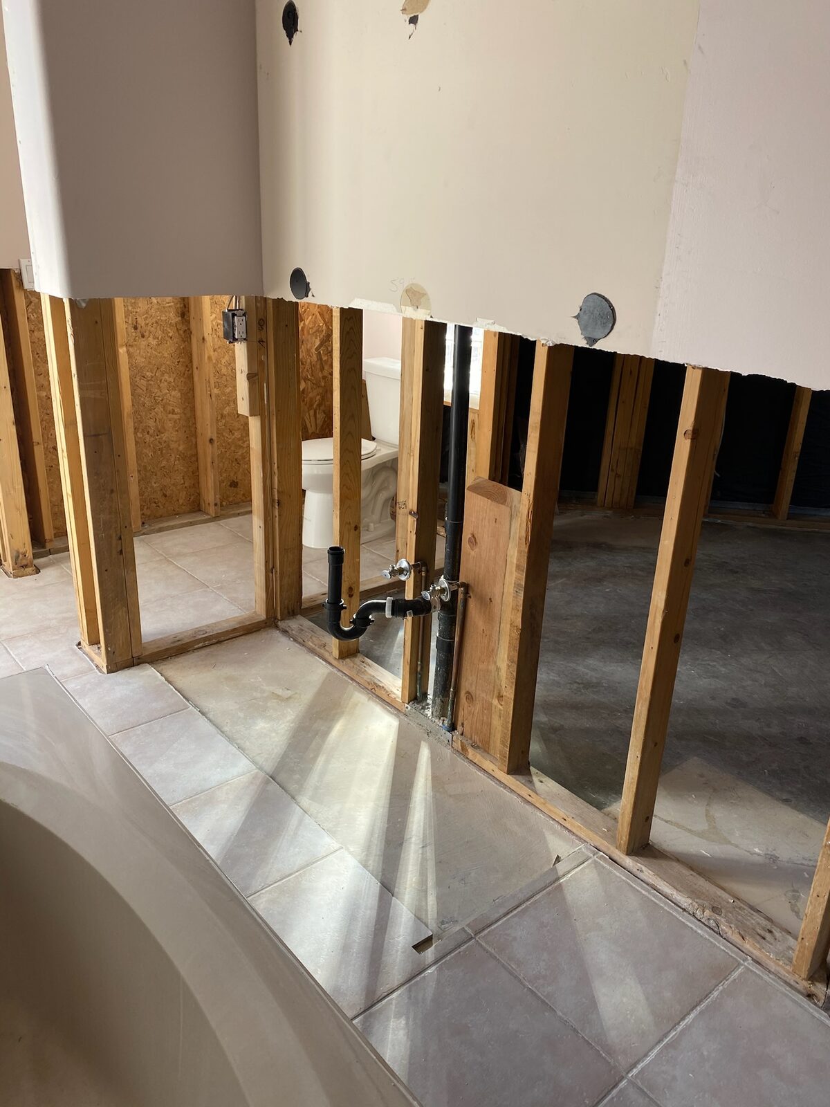 Bathroom walls removed to studs with drain plumbing exposed near a tub deck