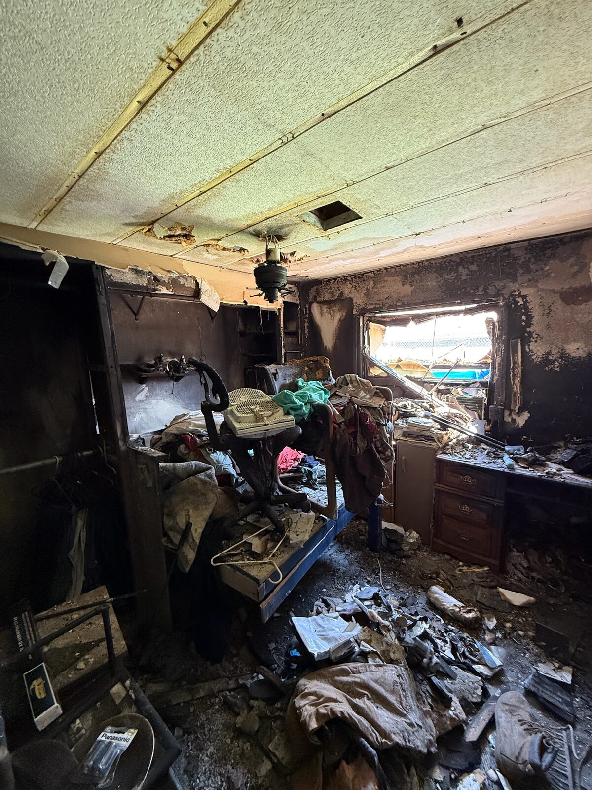 Bedroom interior with heavy fire and smoke damage to walls, ceiling, and contents