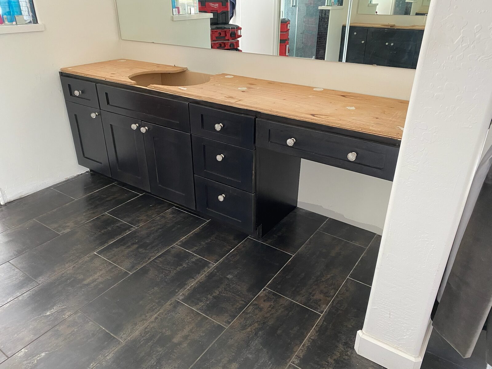Black vanity cabinets with a plywood countertop template installed over dark plank tile flooring