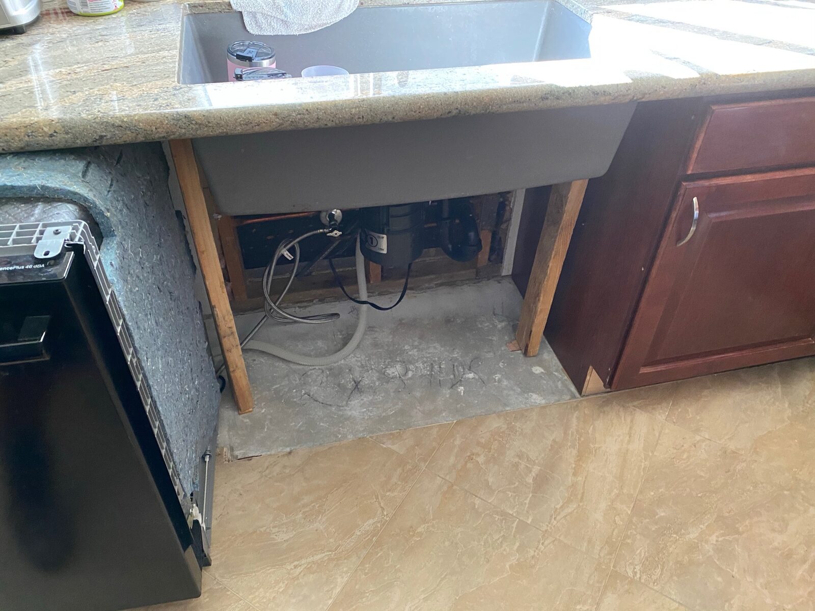 Cabinet removed under a farmhouse sink exposing plumbing and subfloor during repair