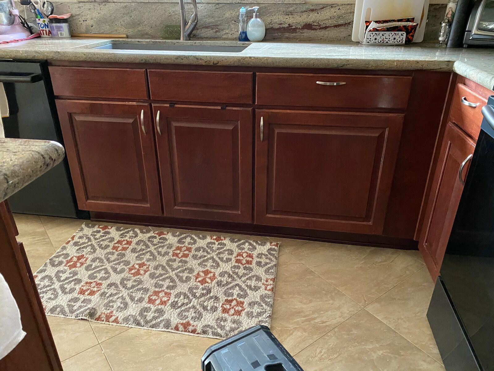Cherry-toned sink base cabinets with brushed handles under a granite countertop