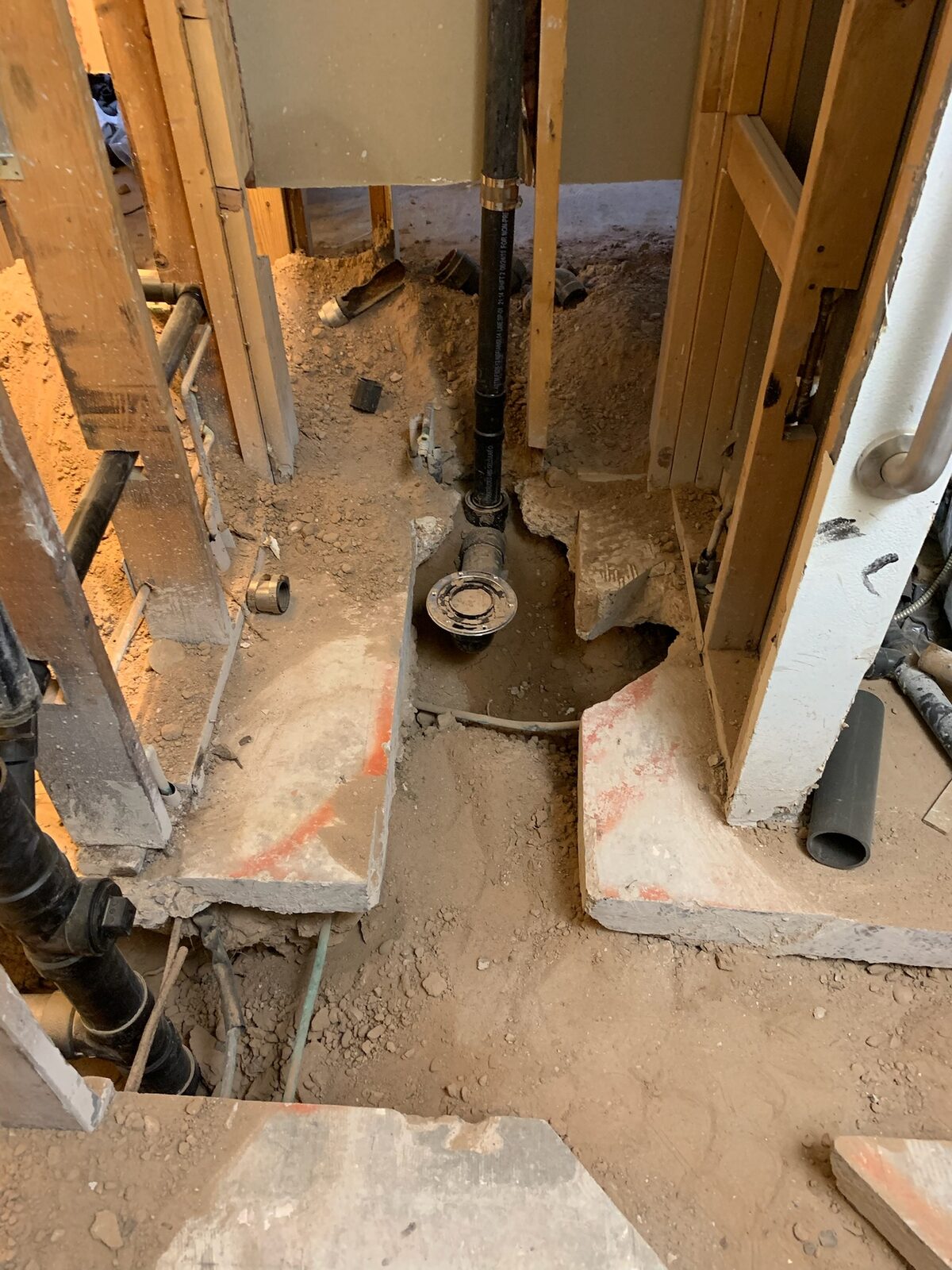 Concrete slab trenched for drain replacement with a new shower drain set between wall studs