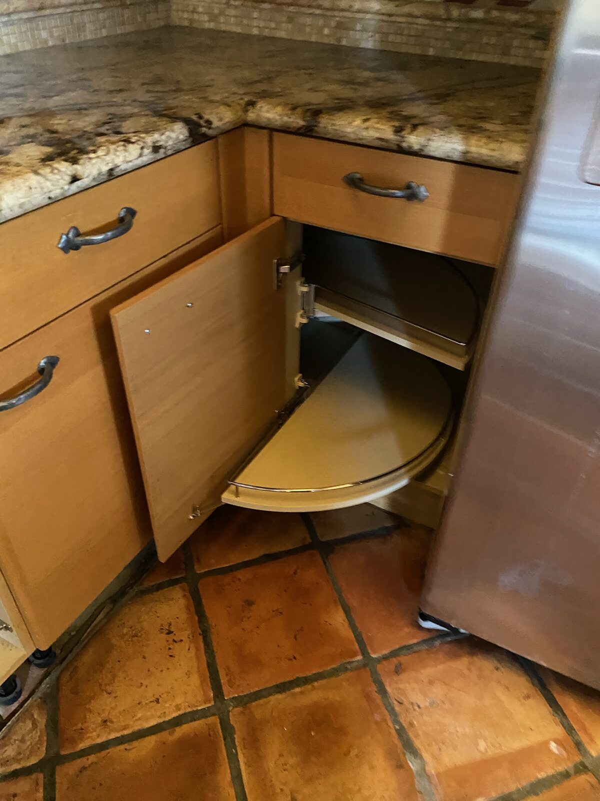 Corner base cabinet with a rotating half moon pull out shelf beside a granite countertop