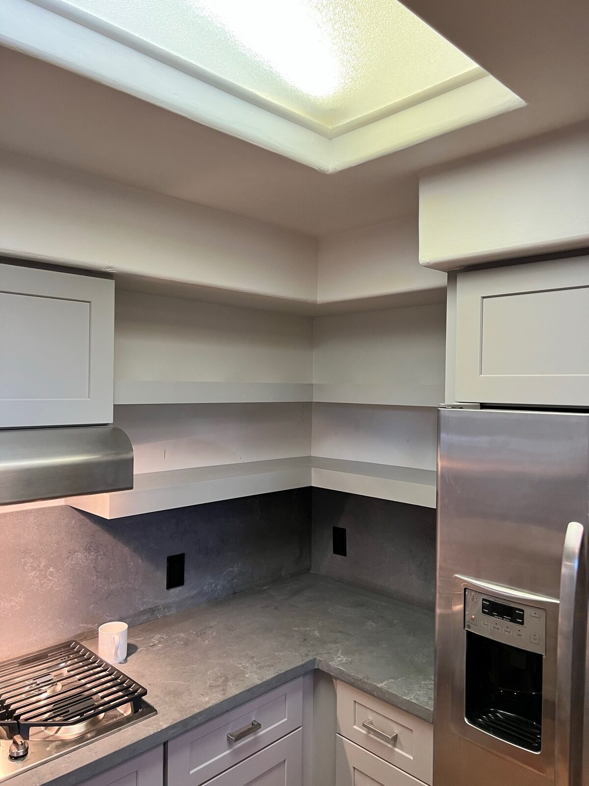 Corner of a remodeled kitchen with slab backsplash, stainless hood, and skylight above