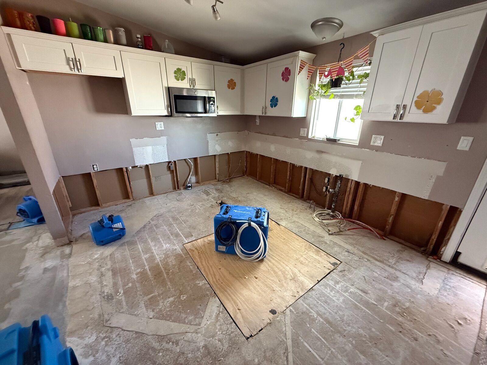 Dehumidifier and air movers drying a kitchen with lower cabinets and flooring removed
