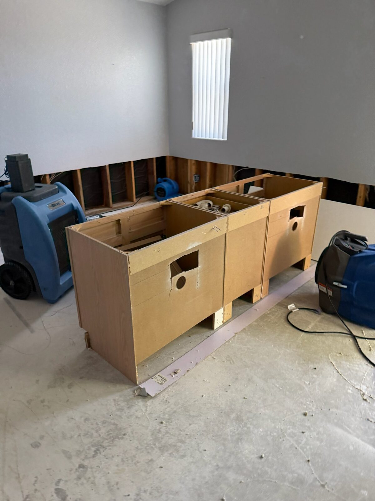 Detached cabinet boxes staged in a room with drying equipment and flood cut walls