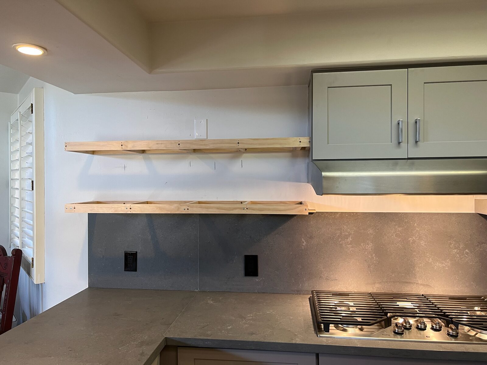 Floating shelf frames mounted above a slab backsplash and gas cooktop in a kitchen remodel