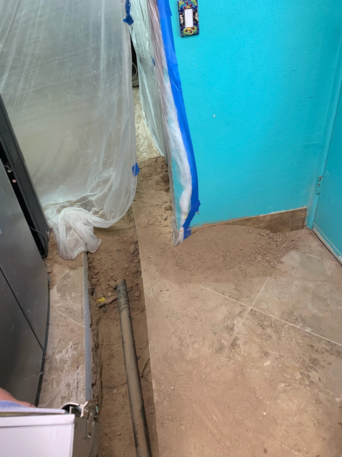 Floor trench dug along a wall for plumbing access with containment plastic hung nearby