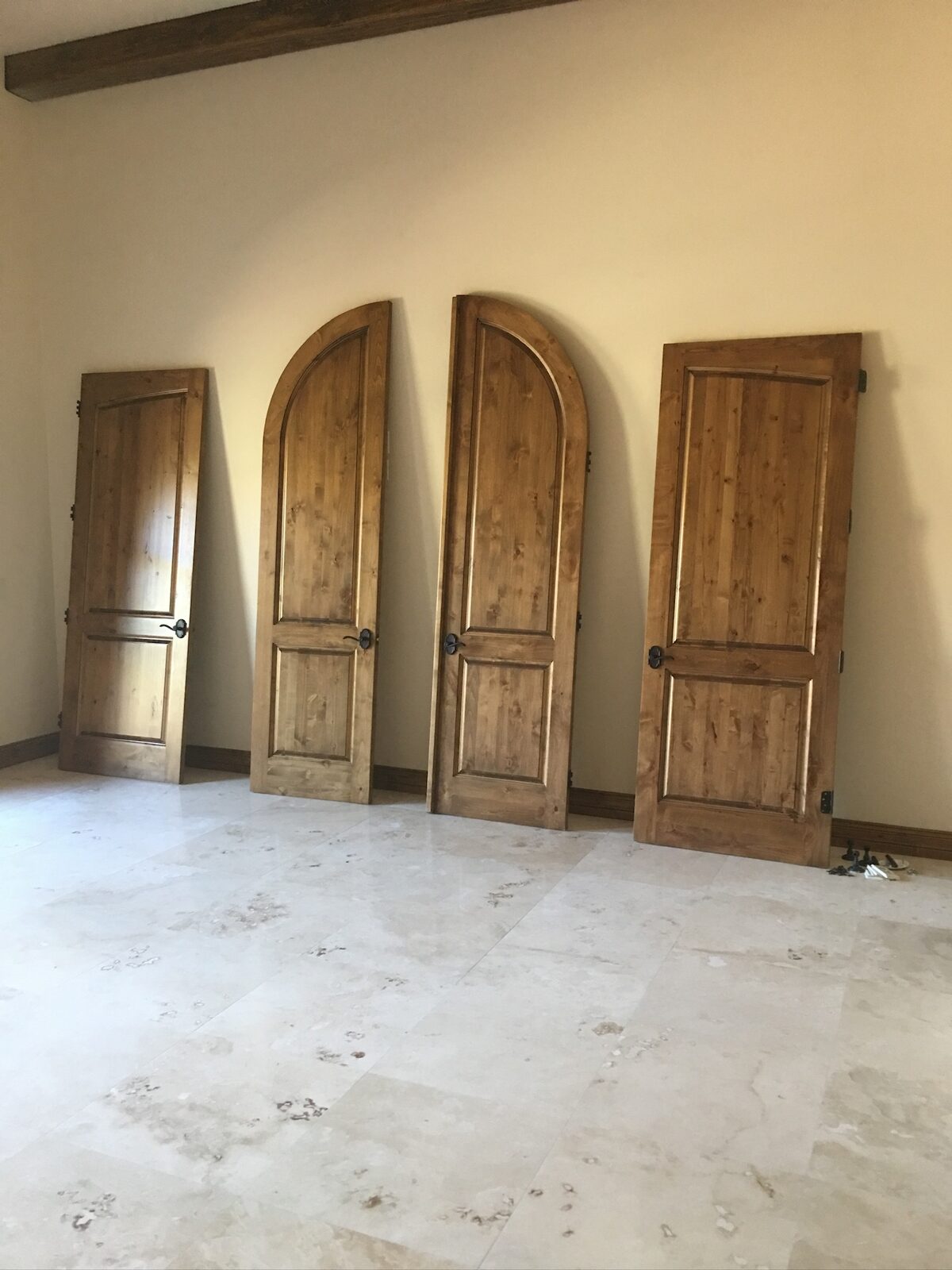 Four stained knotty alder doors, two with arched tops, staged against a wall before hanging