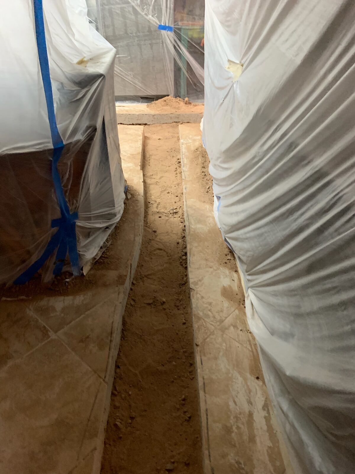 Furniture wrapped in protective plastic beside a floor trenched for plumbing work