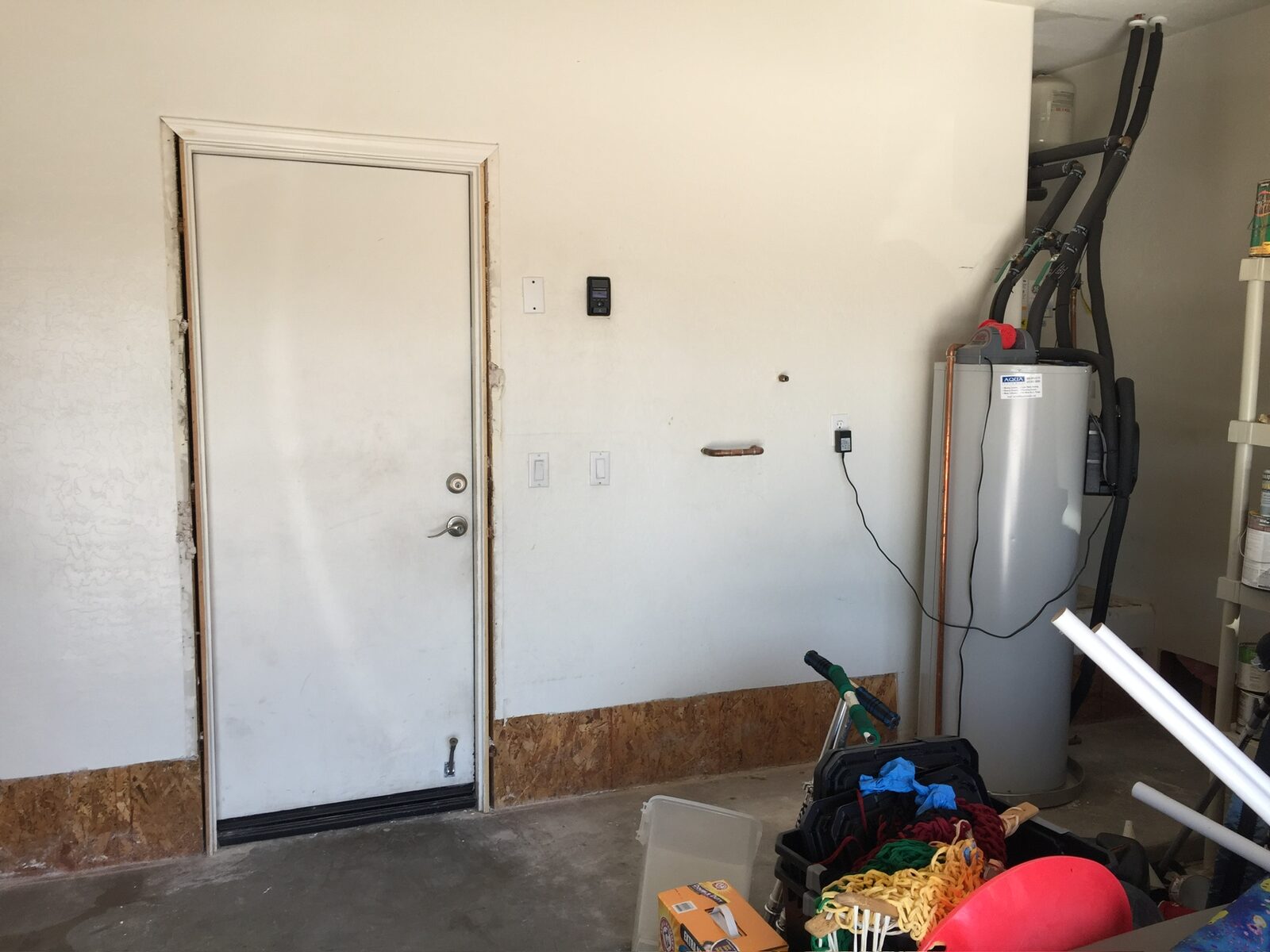Garage wall with lower drywall replaced by exposed sheathing next to a water heater
