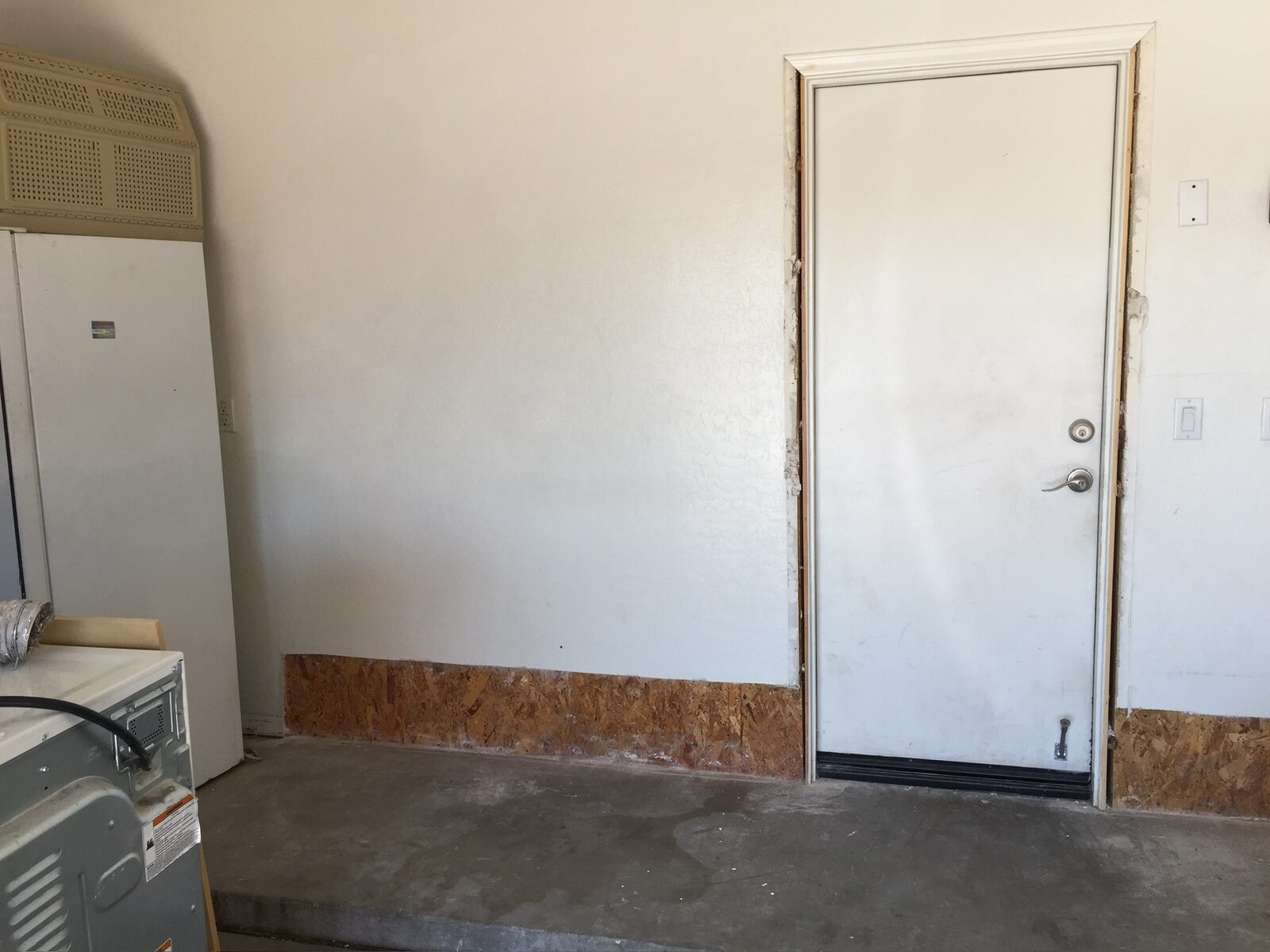 Garage wall repaired with new drywall above an exposed strip of wood sheathing
