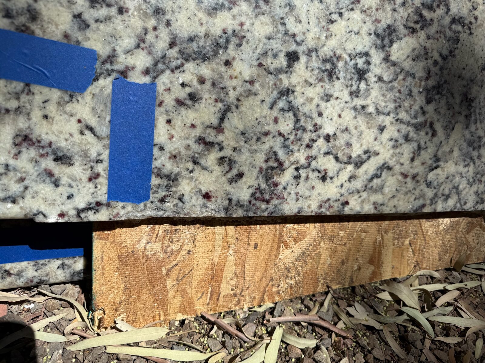 Granite countertop slab edge with painter's tape resting on a wood support outdoors