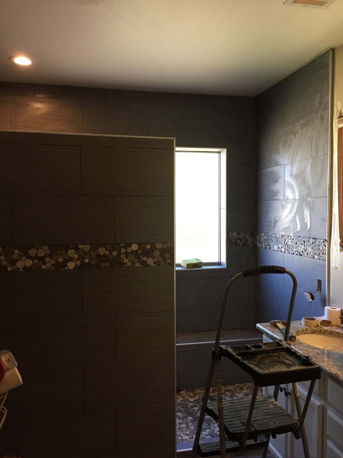 Gray plank-look wall tile with a pebble accent band installed in a shower during a bathroom remodel