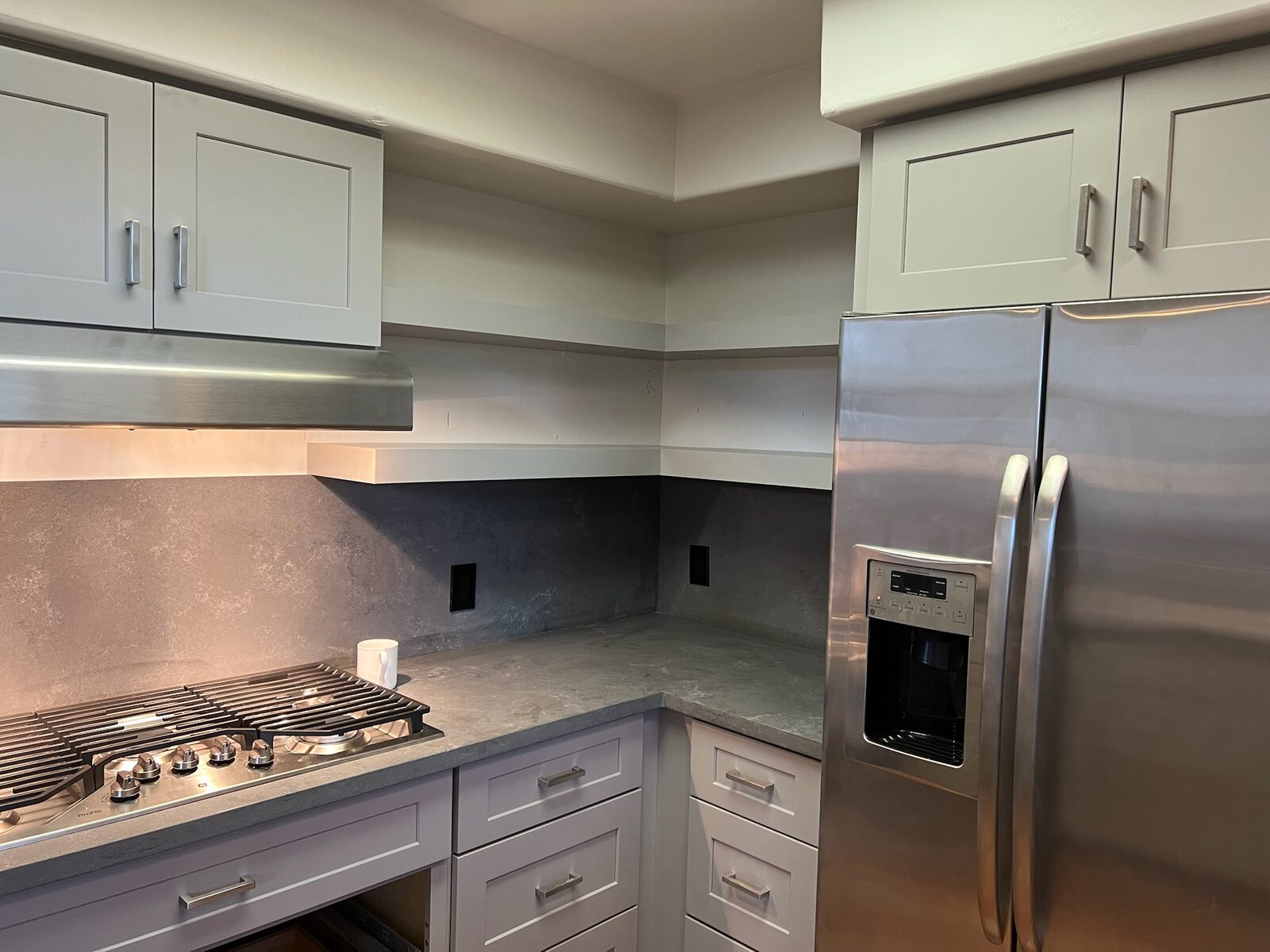 Gray shaker cabinets, stainless range hood, and stone slab backsplash in a kitchen remodel