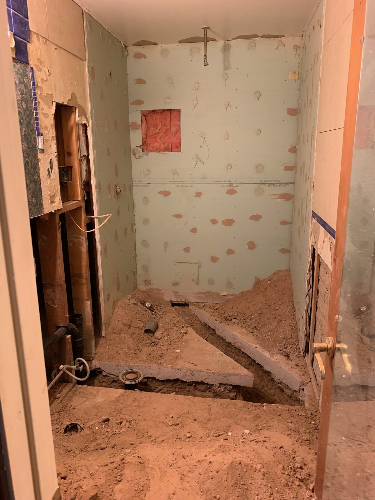 Gutted bathroom with floor slab opened and broken up for plumbing replacement