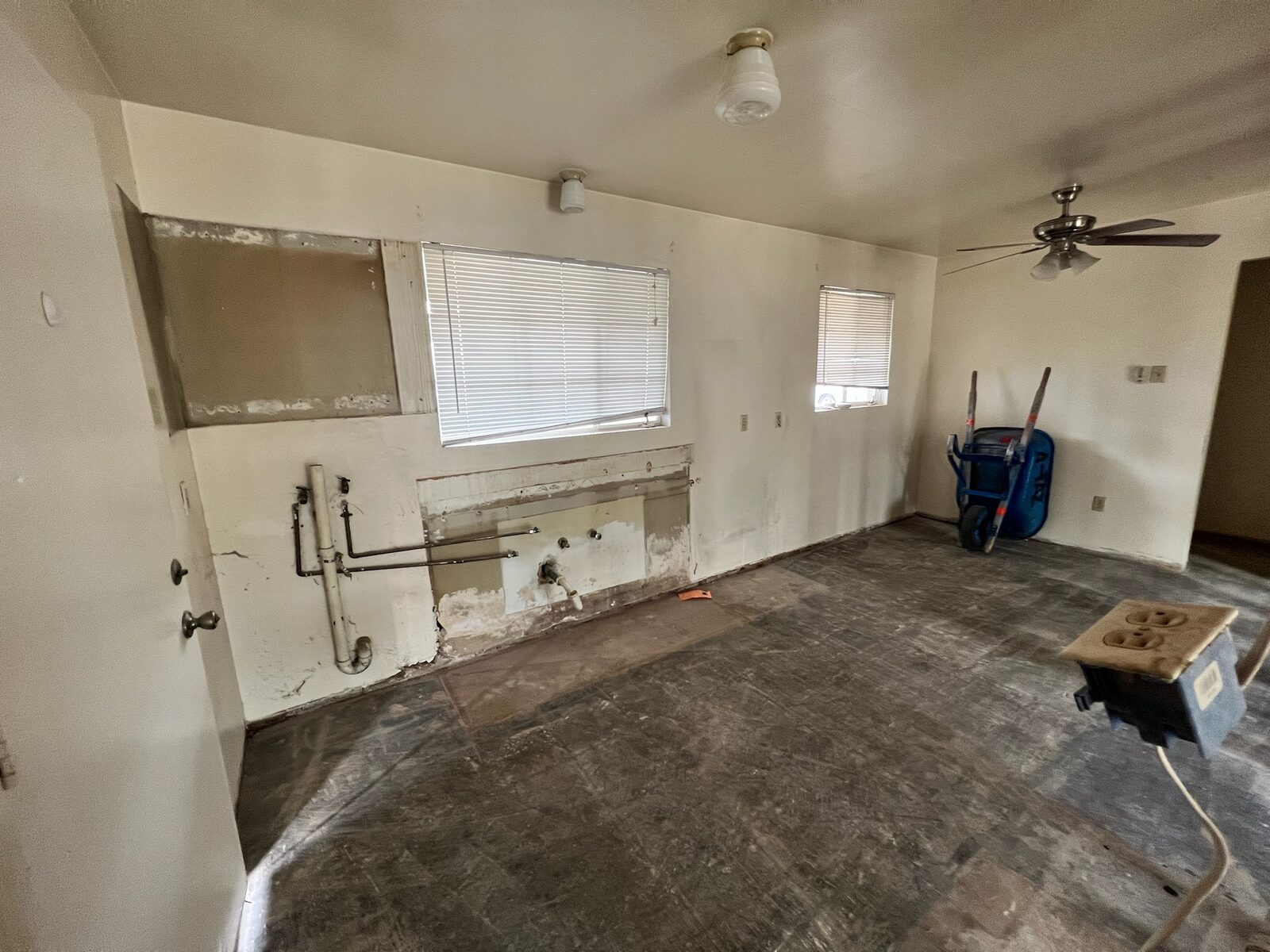 Gutted room with capped plumbing lines and adhesive covered subfloor prepared for rebuild