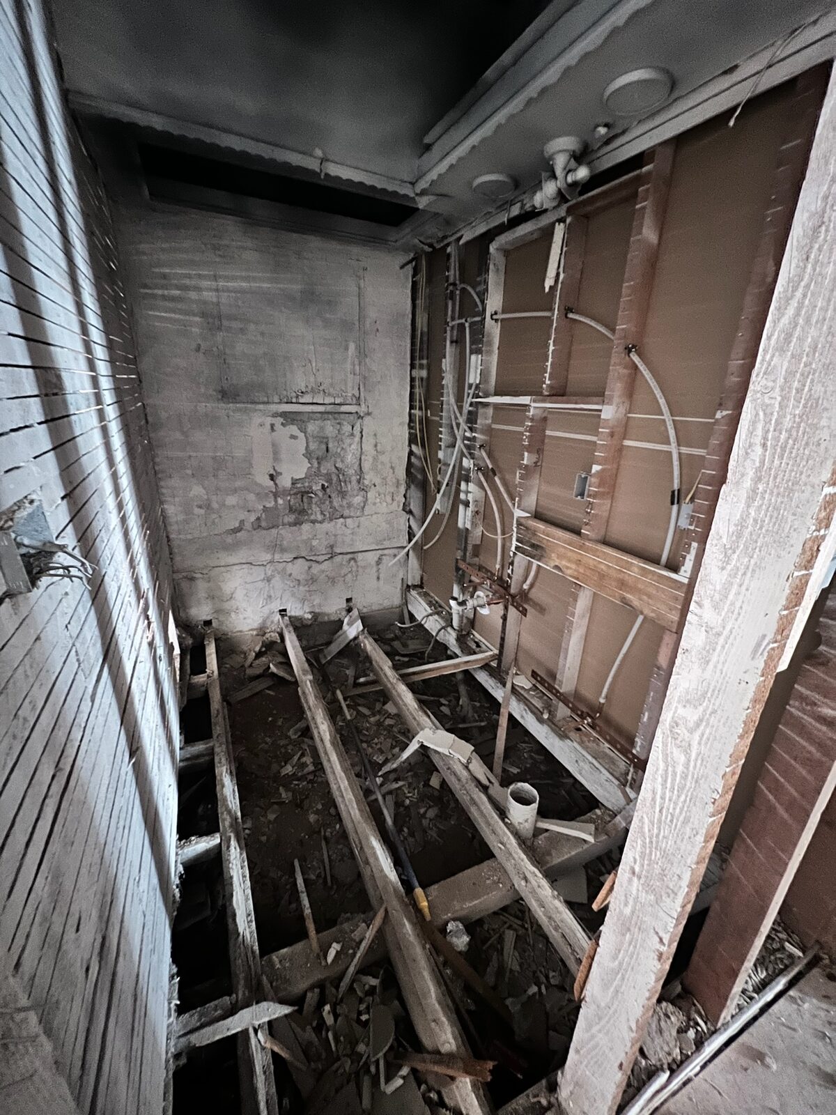 Gutted room with exposed wall framing, floor joists, and debris during demolition