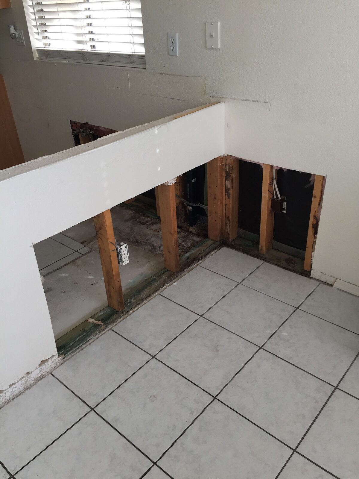 Half wall with lower drywall removed exposing studs and outlets beside a tile floor