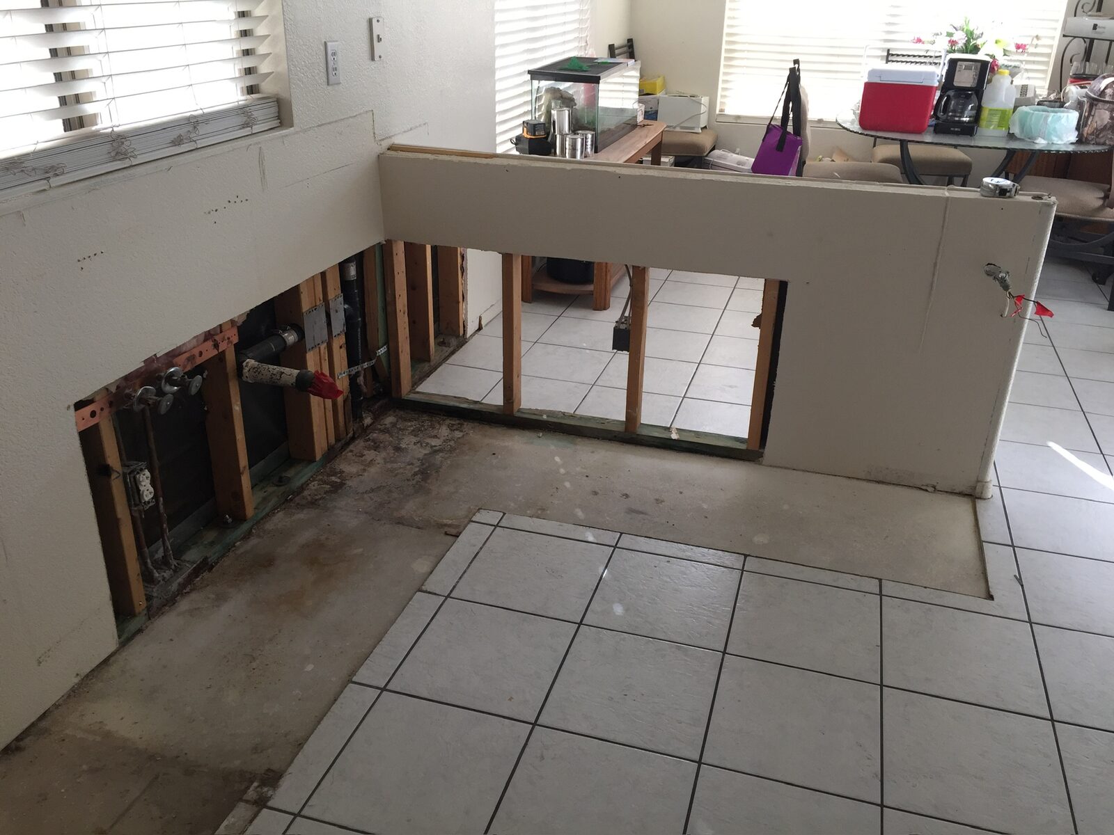Half wall opened to framing with plumbing exposed and adjacent floor tile removed