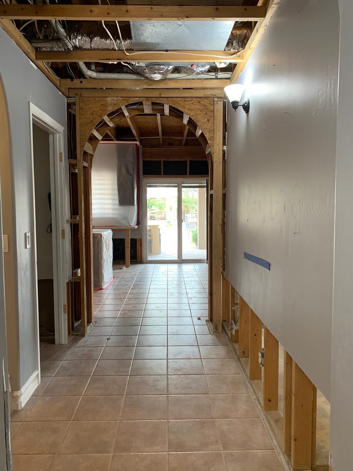 Hallway stripped to framing with an arched opening and exposed ceiling joists