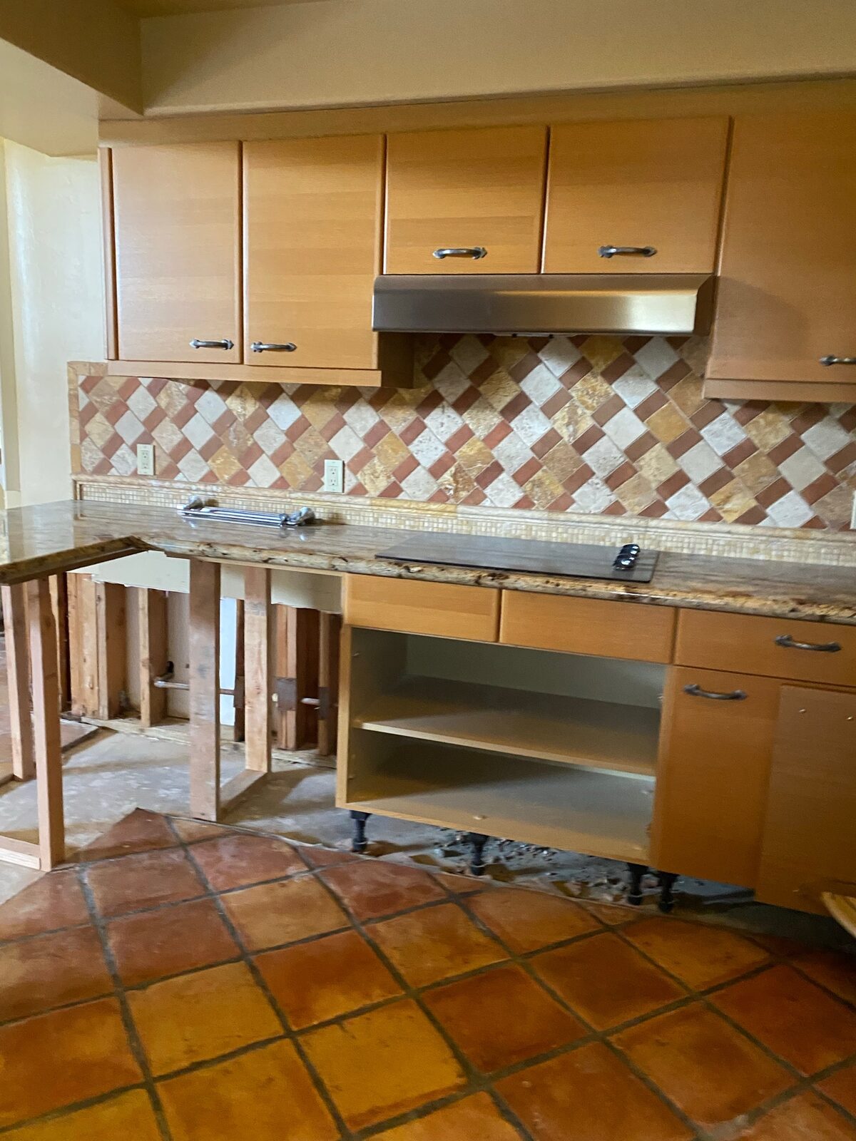 Kitchen base cabinets partially removed below a granite countertop with wall studs exposed