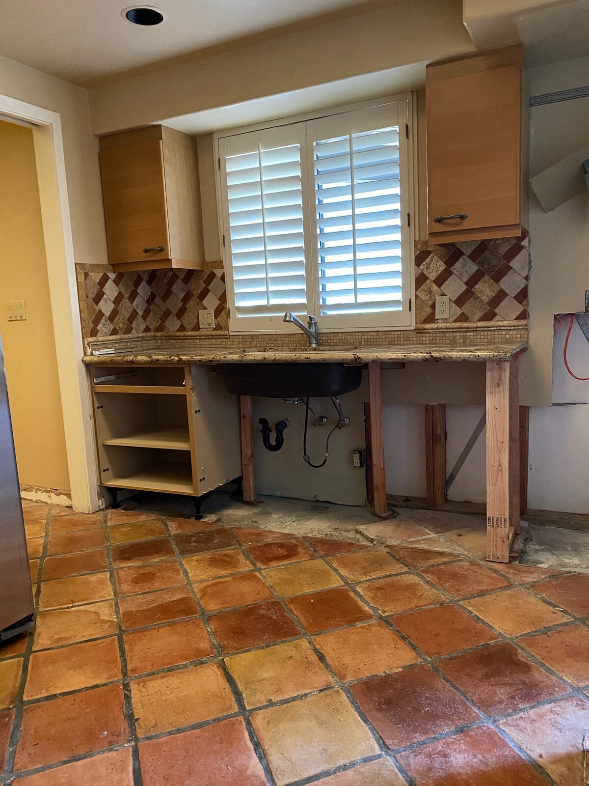 Kitchen sink cabinet removed with granite countertop supported on temporary lumber legs
