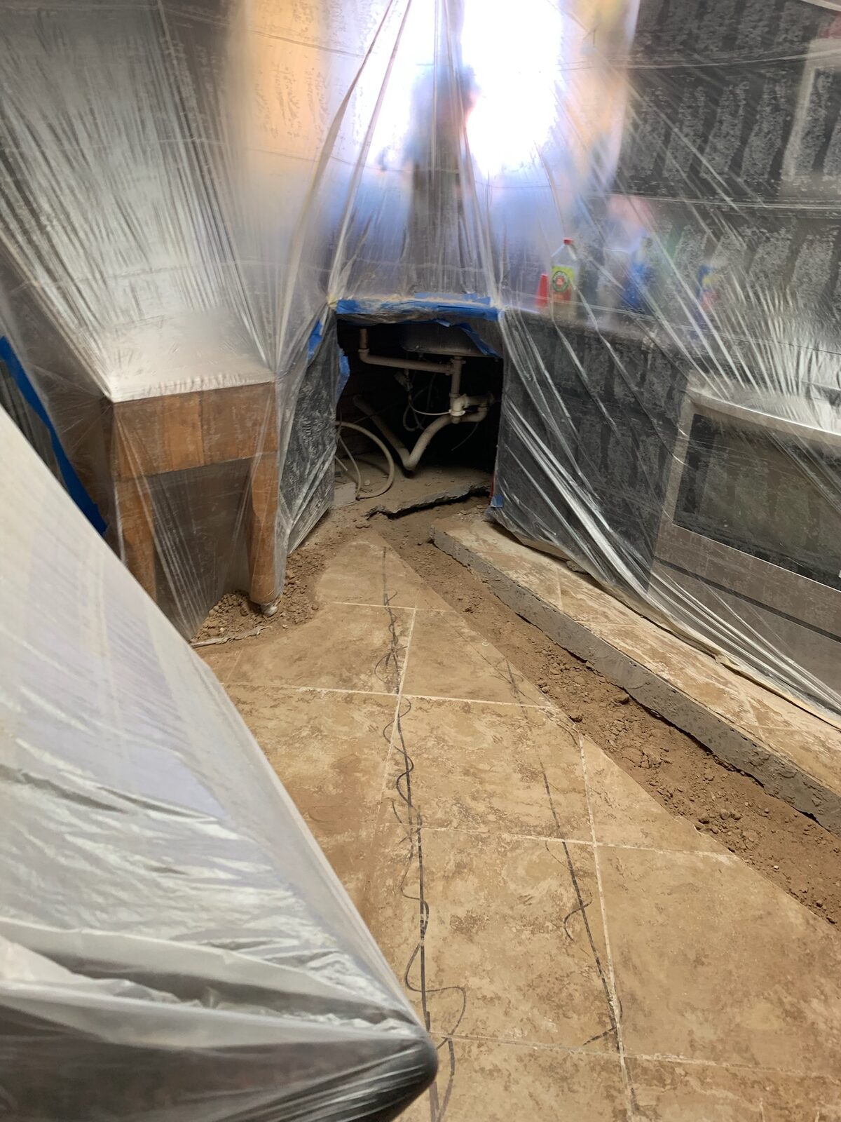 Kitchen under plastic containment with floor tile removed and a trench cut into the slab